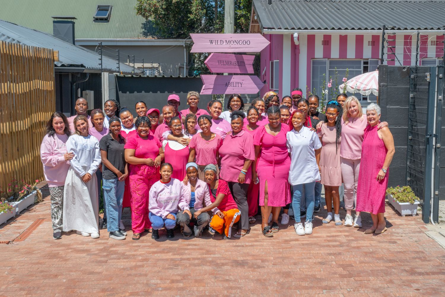 The Wild Mongoo team of women outside their pink George workshop beneath the Vulnerability to Ability signpost, every piece handmade in George