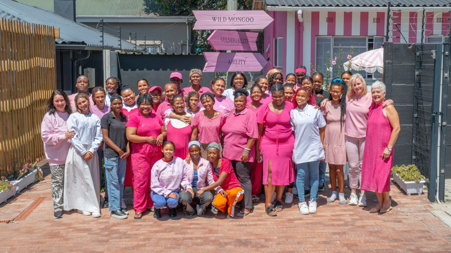 The Wild Mongoo team of women outside their pink George workshop beneath the Vulnerability to Ability signpost, every piece handmade in George
