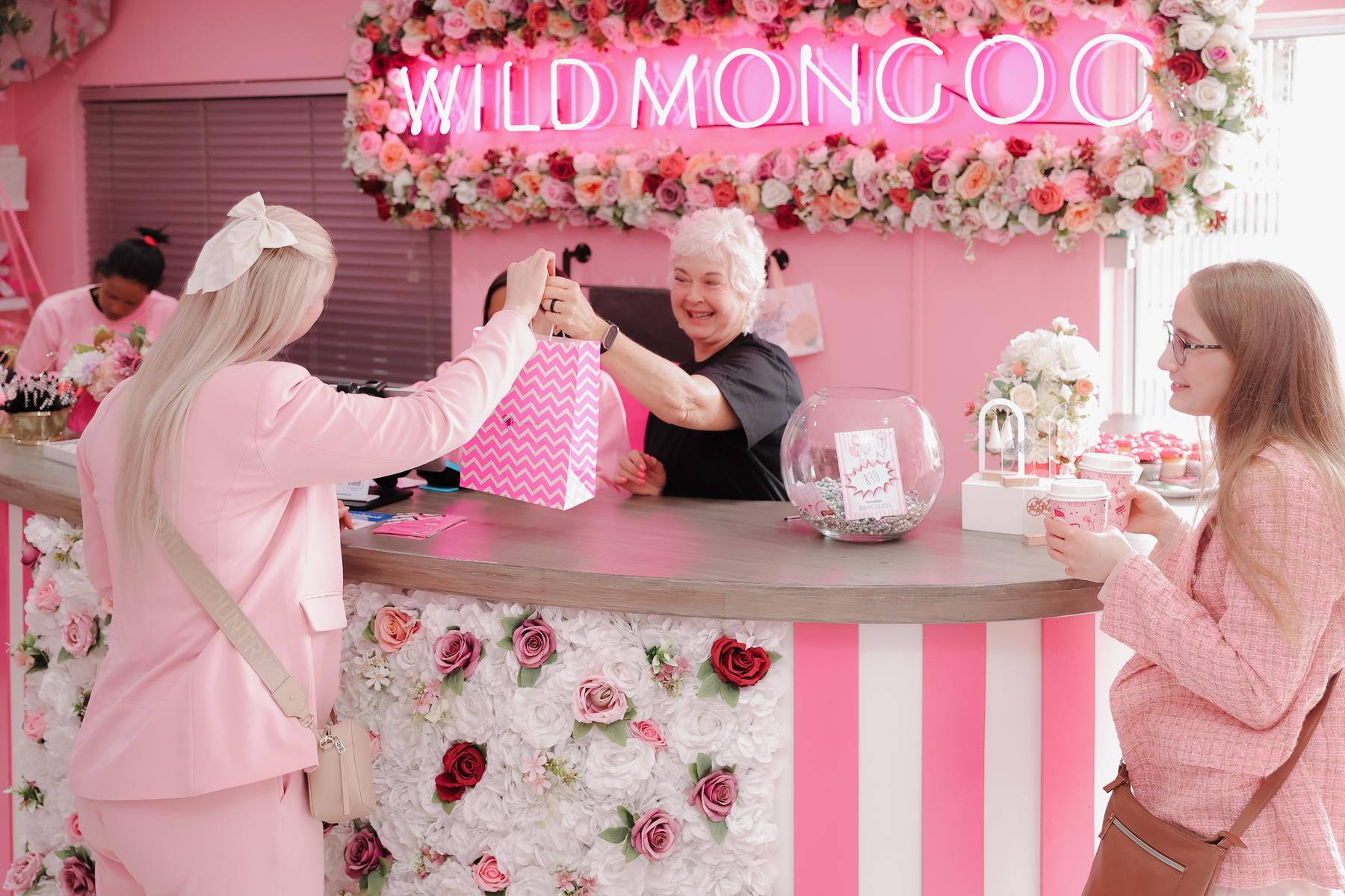 A customer being handed a pink Wild Mongoo gift bag across the flower-covered counter in the George shop, under the neon sign